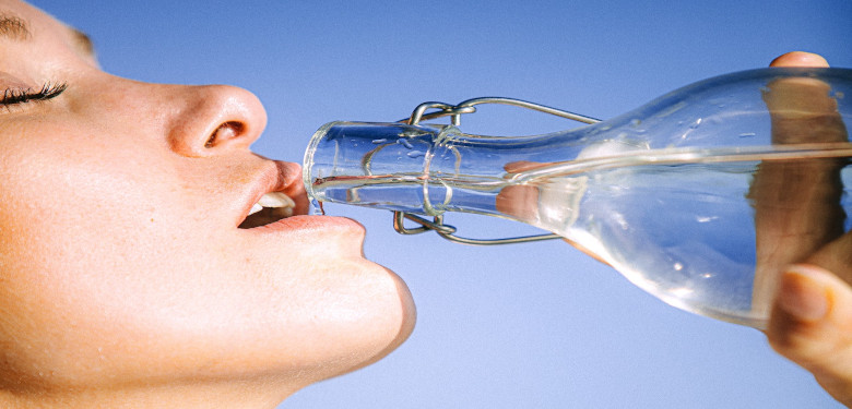 Gesicht einer Frau, die Wasser aus einer Glasflasche trinkt für ausreichend Hydratation nach der Sauna