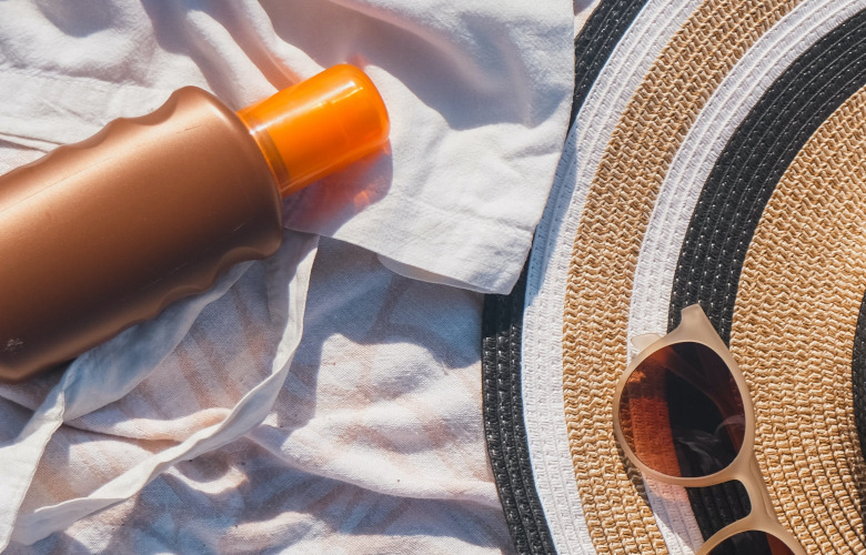 Sonnencreme-Flasche und Hut auf einem Handtuch